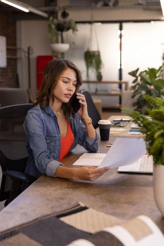 Businesswoman multitasking with smartphone and documents in modern office