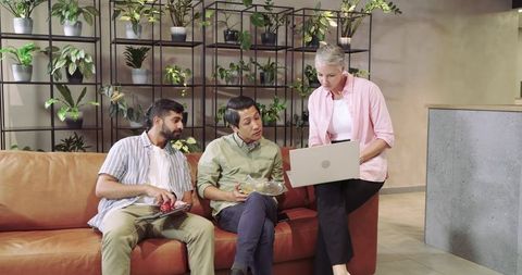 Diverse coworkers collaborating in office lounge with laptop