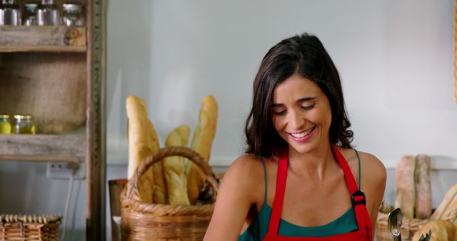 This image showcases a female baker joyfully preparing bread, wearing a red apron in a bakery setting. Suitable for articles or advertisements related to food preparation, professional baking, culinary arts, or bakery promotions. It effectively conveys themes of quality, expertise, and enjoyment in the culinary workplace.