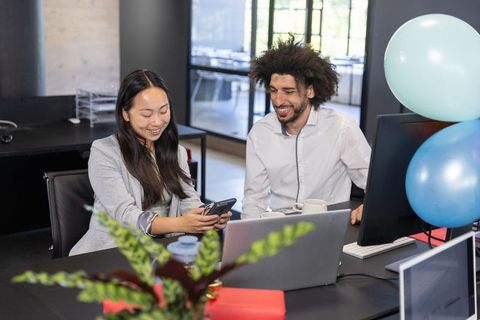 Coworkers Collaborating Near Office Desk with Balloons in Modern Workspace