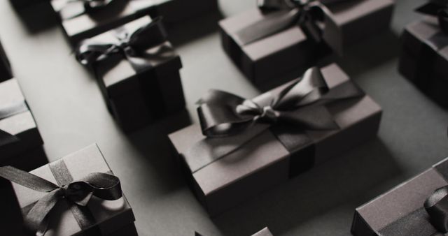 Premium image showcasing a selection of neatly wrapped black gift boxes adorned with black ribbons set on a dark background. Ideal for marketing materials advertising gift packaging services, online stores, luxury product packaging, as well as for blog posts and articles discussing elegant gift ideas, celebrations, or special events.