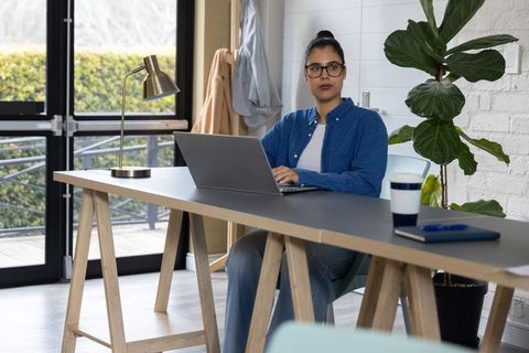 Indian professional woman typing on laptop at minimalist modern home office with plant