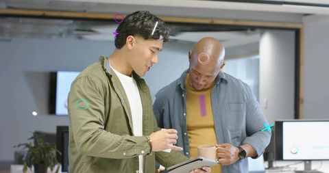 Coworkers collaborating over tablet in modern office holding mug and reviewing data