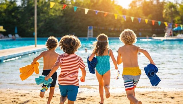 Children running into pool on sunny summer day holding towels and goggles