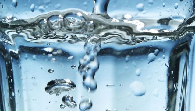 Crystal clear water pouring into glass forming rising bubbles and rippling reflections