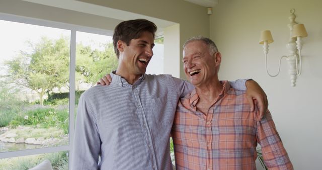 Father and son sharing a joyful moment at home, smiling and embracing each other. Could be used for family, happiness, relationships. Ideal for advertisements or articles focusing on family bonds, quality time, or positive emotions.