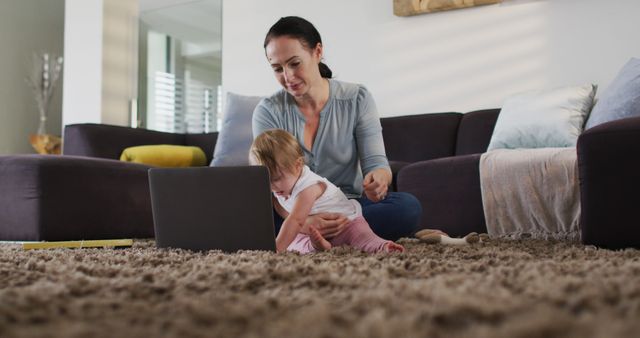 Woman sitting on carpeted floor, using laptop while her young child interacts with computer. Scene depicts modern parenthood and the juggling of work responsibilities with childcare at home. Ideal for articles or adverts targeting work-life balance, remote work, or parenting topics.