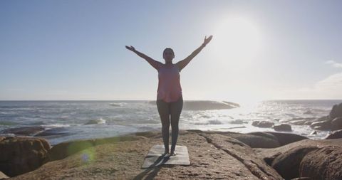 Woman Practicing Yoga on Rocky Ocean Coastline at Sunrise