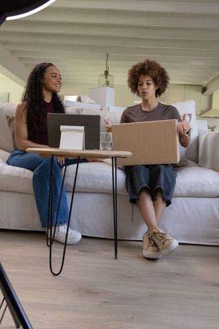 African american friends unboxing package on couch while using tablet for online review