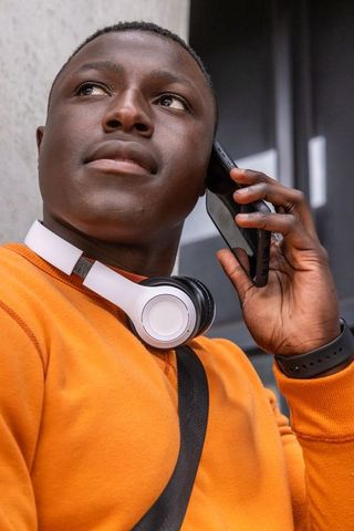 African american man talking on smartphone with white headphones wearing orange sweatshirt
