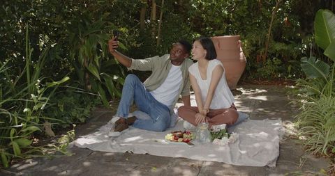 Couple Taking Selfie on Picnic Blanket in Lush Garden