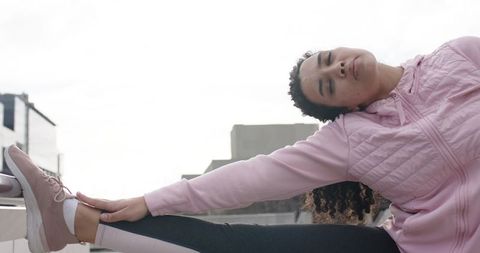 Young woman stretching leg on rooftop parapet in pink quilted jacket