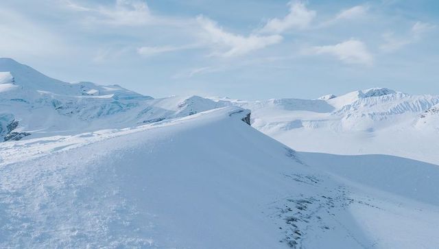 Wind-sculpted snow ridge on glacial plateau with curved cornice and alpine vastness