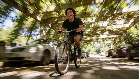 Joyful man riding city bike under sunlit pergola with motion blur urban cycling