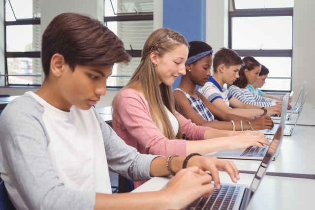 Group of diverse students using laptops in a classroom setting. Ideal for articles or advertisements about modern education, collaborative learning, and technology integration in schools. Suitable for use by educational institutions, technology in education platforms, and academic resources websites.