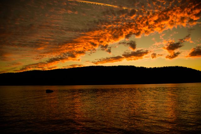 Dramatic sunset with vivid colors in the sky reflecting on a calm lake offering peaceful and serene vibes. Ideal for nature-themed designs, travel brochures, desktop wallpapers, relaxation video series, or meditation app backgrounds.