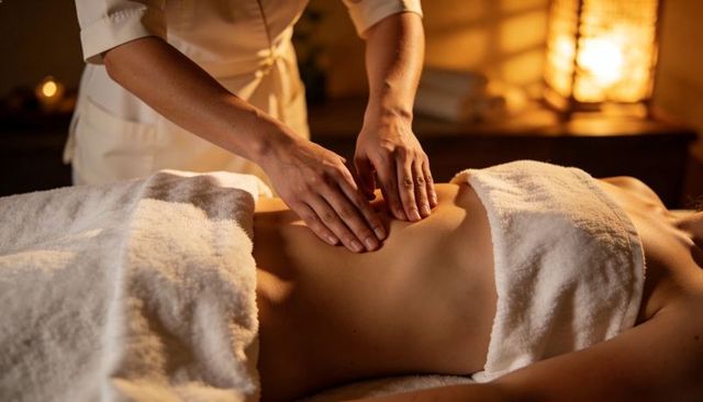 Wellness spa therapist massaging client abdomen under warm candlelight for deep relaxation