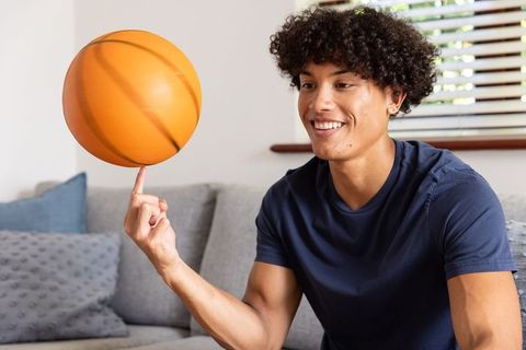 Young Man Spinning Basketball on Finger Sitting on Couch in Living Room