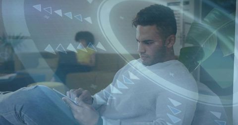 Asian man tapping tablet in coworking lounge, scrolling with futuristic HUD overlays