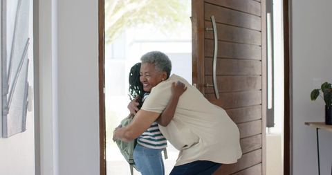 Grandmother hugging granddaughter at sunlit entryway warm homecoming embrace