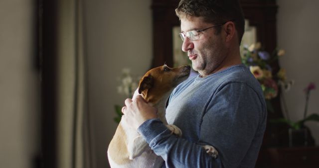 Caucasian man standing at window, petting dog and smiling at home - Download Free Stock Photos Pikwizard.com