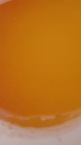 Shining amber liquid settling in cup closeup with foamy rim and speckled glossy surface