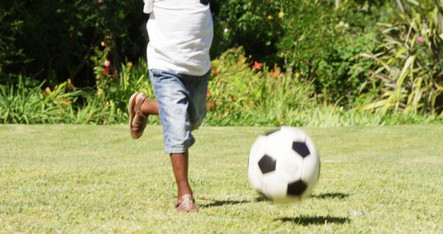 A child is playing soccer on a lush green field, kicking a ball with energy and focus. Capturing the essence of youth and sports, the image reflects the joy and activity of outdoor play.