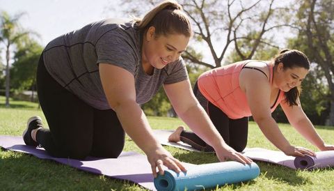 Plus-size women unrolling yoga mats in sunny park preparing for outdoor fitness session