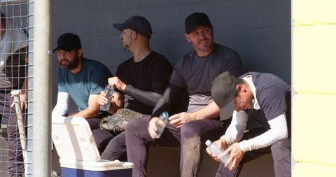 Baseball players resting in dugout drinking water between innings on sunny afternoon
