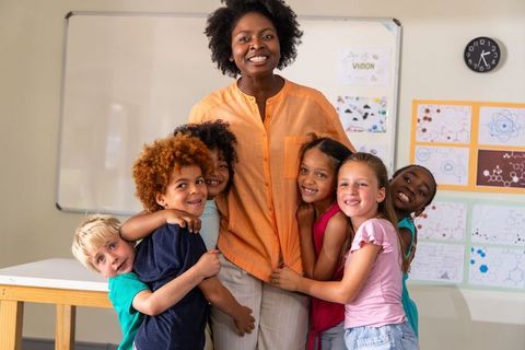 African american teacher hugging diverse primary school children during classroom celebration