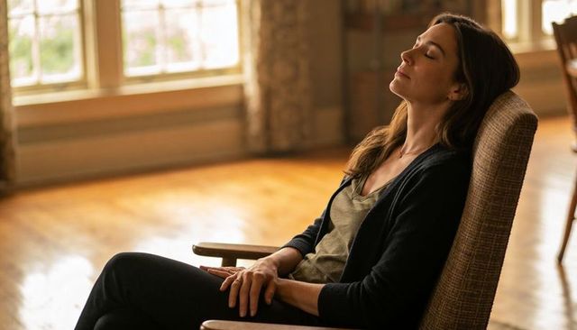Woman relaxing in armchair by sunlit window with closed eyes, calm home interior