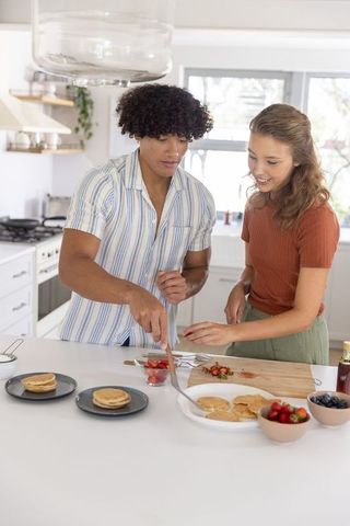 Diverse couple preparing and plating pancakes at bright modern kitchen island smiling