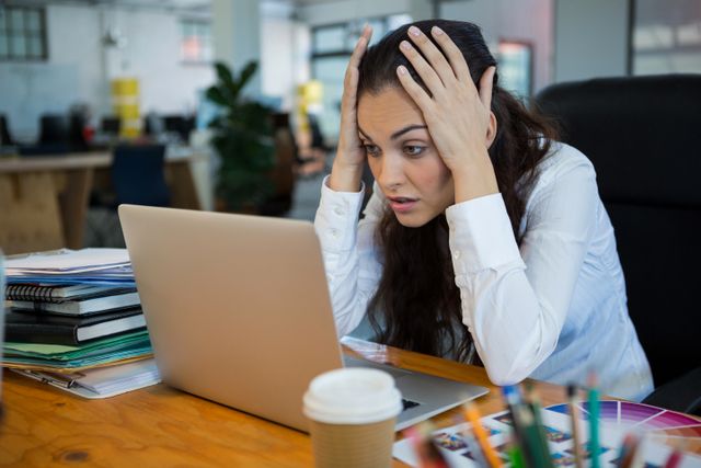 Upset female graphic designer looking at laptop in office