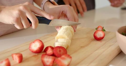 Couple slicing banana and strawberries on wooden cutting board preparing healthy breakfast