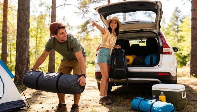 Couple unloading camping gear from suv at sunny forest campsite carrying tent and backpack