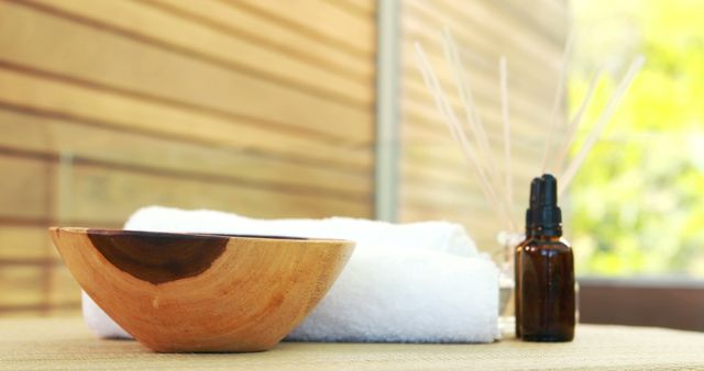 A wooden bowl and a white towel are neatly placed on a surface, suggesting a serene spa environment, with copy space. The essential oil bottle adds to the tranquil ambiance, indicating a setting for relaxation and wellness.