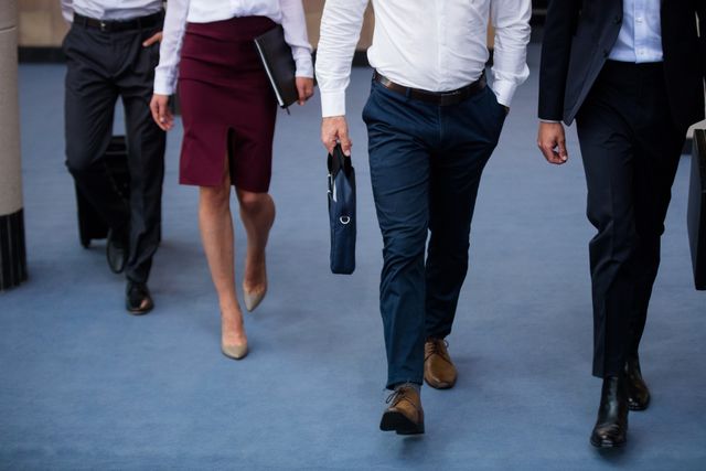 Group of business executives walking together in a conference center lobby. Ideal for illustrating concepts of teamwork, corporate environment, business meetings, and professional attire. Suitable for use in business presentations, corporate websites, and marketing materials.