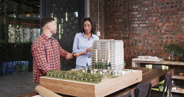 Architects engage in discussion while examining a detailed building model in a contemporary office workspace. Ideal for articles on architectural processes, teamwork in design, urban planning, and modern work environments. Suitable for business presentations, design firm marketing, and collaborative project case studies.