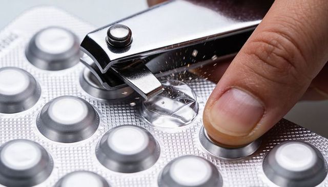 Nail-clipper puncturing blister pack releasing powder, close-up of pill packaging damage