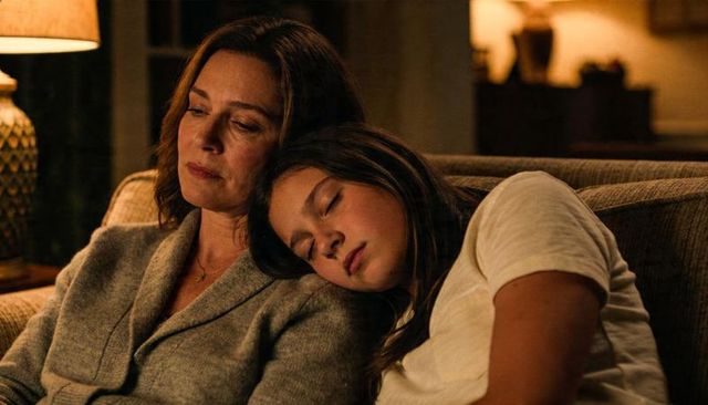 Mother cradling sleeping daughter on sofa in warm evening light, intimate family moment