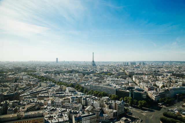 Panoramic shot of Paris skyline featuring the Eiffel Tower in the center under blue skies on a sunny day. Ideal for use in travel brochures, tour advertising, online articles about French tourism, postcards, desktop wallpapers, or as wall art decor in home or office spaces.