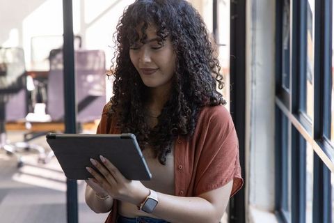 Young woman using tablet in modern coworking space by window wearing smartwatch