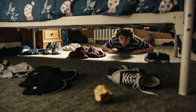 Teen crawling under bed in messy bedroom with scattered clothes, sneakers and apple core