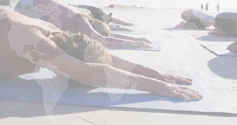 Women stretching on beach yoga mats with world map overlay, outdoor group fitness