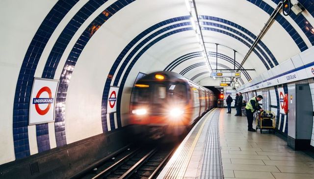 Underground train entering curved london platform with hi-vis workers and commuters