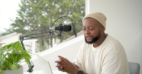 African american man recording podcast at home desk with microphone boom arm pop filter