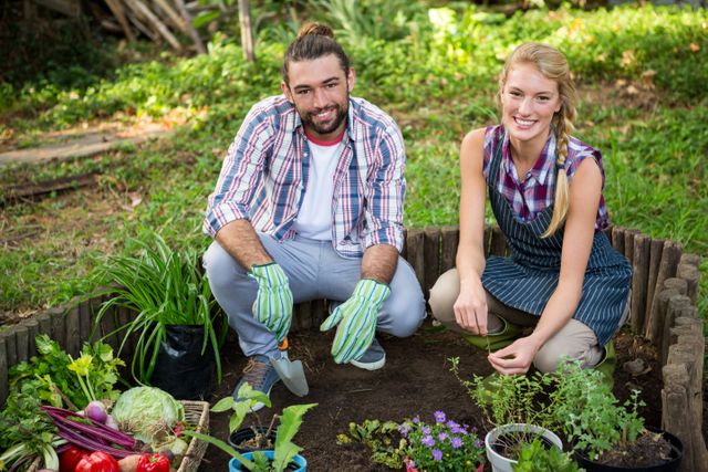 Portrait of happy young gardeners crouching with potted plants at garden