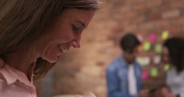 Smiling Woman in Office with Two Colleagues in Background - Download Free Stock Images Pikwizard.com