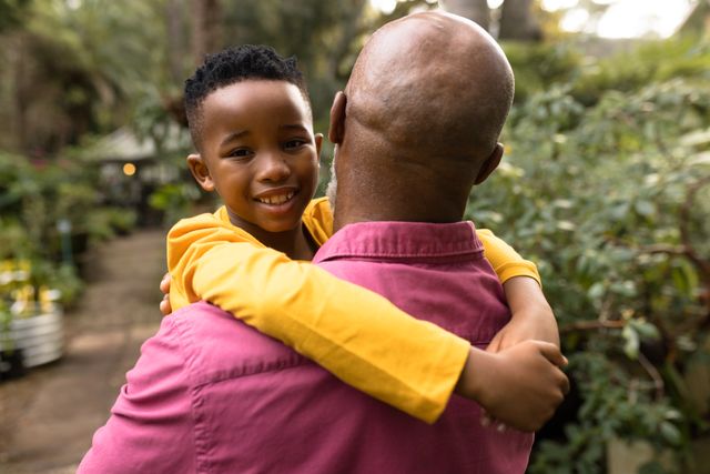 Grandfather and grandson sharing a joyful moment in a lush garden. Perfect for themes of family bonding, multigenerational relationships, outdoor activities, and the beauty of nature. Ideal for use in advertisements, family-oriented content, and lifestyle blogs.