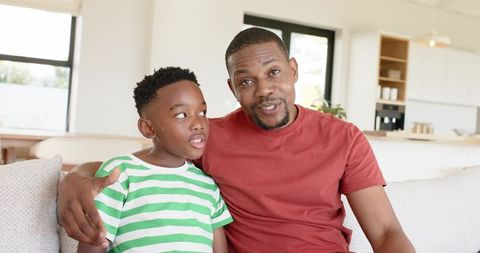 African american father and son sitting on sofa sharing warm moment in bright living room